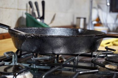 Siyah bir mutfak ocağına yakın, çelik bir sobanın üzerine siyah bir demir tava fırlatılmış.