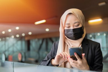 Yeni Normal kavram: Malaylı genç bayan yüz maskesi takıyor ve elinde akıllı telefon var