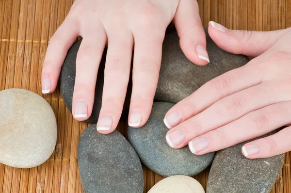 Mãos femininas com manicure francês na pedra em fundo de bambu — Fotografia de Stock