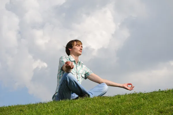 Genç erkekler gökyüzü üzerinde çayır üzerinde meditasyon — Stok fotoğraf