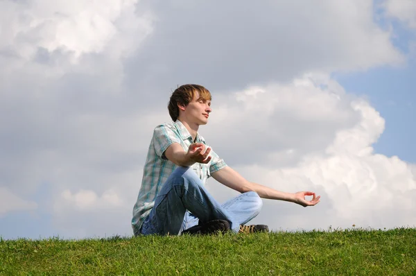 Genç erkekler gökyüzü üzerinde çayır üzerinde meditasyon — Stok fotoğraf