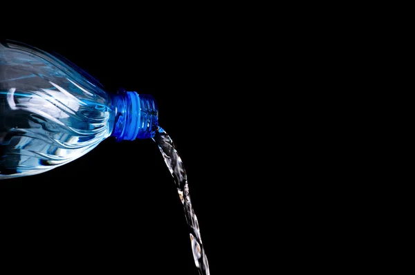 Hälla vatten från en flaska på svart bakgrund — Stockfoto
