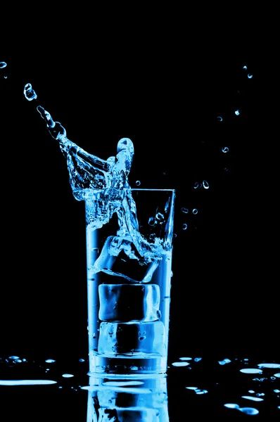 Blaues Wasser plätschert im Glas auf schwarzem Hintergrund — Stockfoto