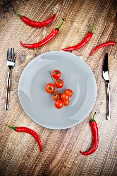 Pimentas vermelhas e tomates no prato em mesa de madeira — Fotografia de Stock