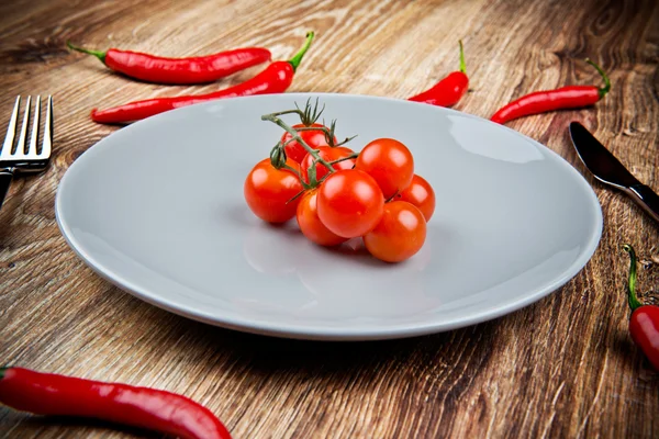 Red hot chili peppers and tomatoes on the plate on wooden table — Stock Photo, Image