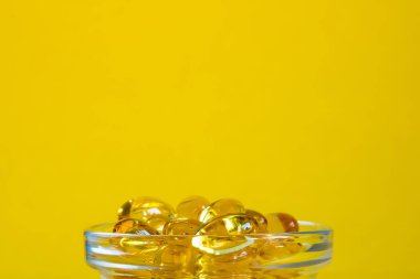 Omega 3 kapsüllü kase sarı arka planda, kopyalanmış alan, yan görünüm