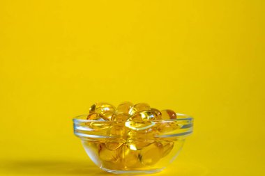 Omega 3 kapsüllü kase sarı arka planda, kopyalanmış alan, yan görünüm