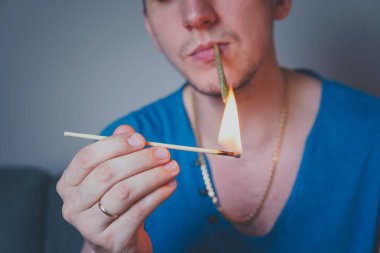 Close-up of adult man lights up with matches and smoking medical marijuana joint. Concept of herbal and alternative medicine