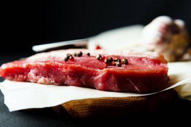 Raw organic beef meat with rosemary, seasonings, salt and red pepper  on black background, close-up. Preparing to cooking steak