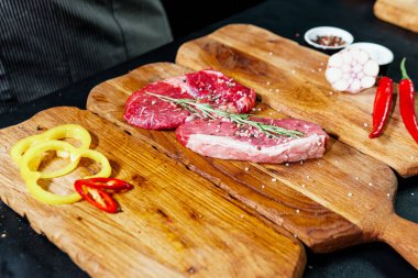 Raw organic beef meat with rosemary, seasonings, salt and red pepper  on wooden cutting board, close-up. Preparing to cooking steak