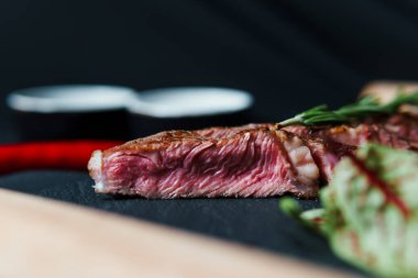 Dilimlenmiş biftek az pişmiş, siyah kesme tahtasında sebzelerle servis ediliyor. Restoran menüsündeki lezzetli et. Yemek şirketi kavramı
