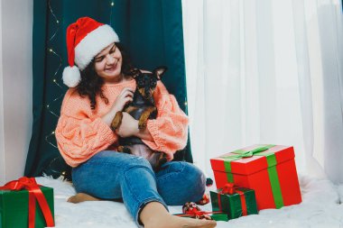 Noel balosu ve hediye kutuları etrafında komik köpek minyatürleriyle oynayan genç bir kadının portresi. Yeni yıl anlayışı