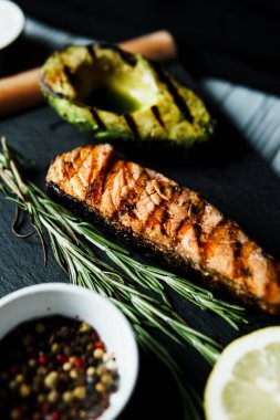 Izgara somon balığı filetosu ve siyah kesim tahtasının üzerinde yeşil salata, yakın çekim. Restoran menüsünde lezzetli yemekler var. Yemek servisi kavramı