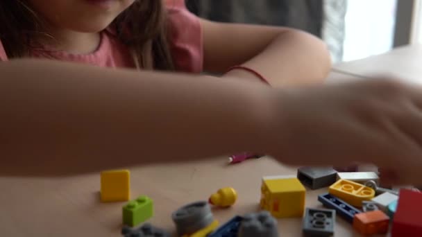 かわいい女の子は木製のテーブルに座っていて カラフルなレゴの建物のブロックで遊んでいます — ストック動画