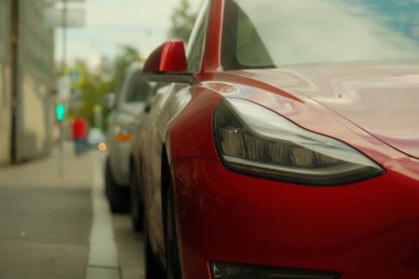 Kaldırımın kenarına park edilmiş kırmızı bir Tesla 'nın sağ ön farını.