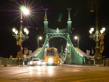 Budapeşte 'deki Özgürlük Köprüsü veya Szabadsg Hd veya Özgürlük Köprüsü' ndeki gece görüşü Buda ve Pest 'i Tuna Nehri' nin karşısına bağlıyor. Bir tramvay ve bir araba köprüden geçer..