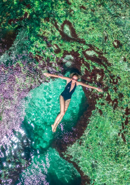 印度尼西亚巴厘岛努沙佩尼达岛上的安格斯比劳岛上，一个美丽的天然水族馆在海岸岩石中，小女孩躺在水里. 免版税图库照片