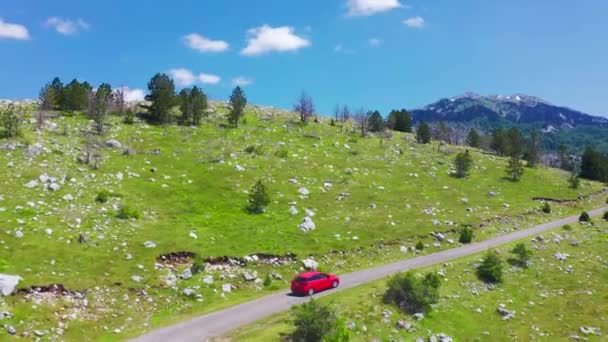 15 juli 2021 - Montenegro. Luchtfoto van de weg met rode auto in prachtige bergen in Komovi, Montenegro. Reisconcept voor auto 's. — Stockvideo