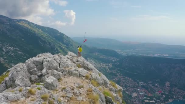 Beberapa pelancong berdiri di puncak gunung yang menghadap kota tua Kotor, Montenegro. Pandangan pesawat tak berawak. Konsep gaya hidup dan perjalanan. — Stok Video