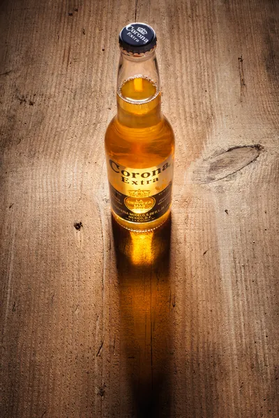 Gold Corona Extra beer bottle with long shadow on wooden boards — Stock Photo, Image