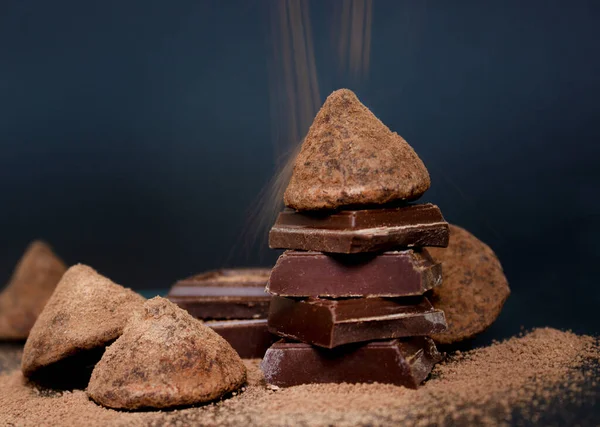 Čokoládové bonbóny lanýže a kousky čokolády a létající kakao prášek na tmavém pozadí — Stock fotografie