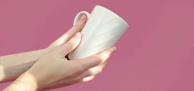 Pembe arka planda beyaz bir bardak tutan kadın elleri. Yiyecek içecek konsepti. Boşluğu kopyala.