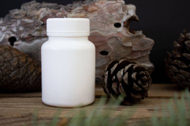 Siyah arka planda ağaç kabuğu ve ladin dallarıyla beyaz plastik bir kavanozun maketi, güzellik ürünü ambalajlama.
