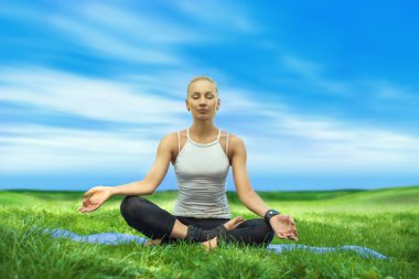 Yoga kadın mavi gökyüzü üzerinde yeşil çimenlerin üzerinde