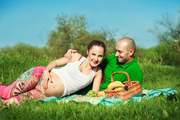 Jonge gelukkig zwangere vrouw met jonge man liggend op het gras hav — Stockfoto