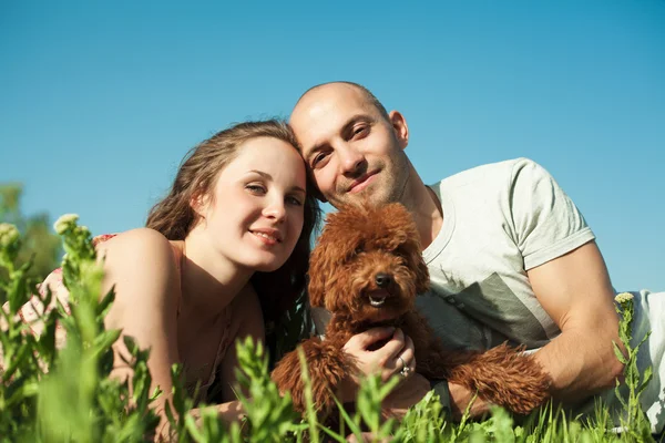 Retrato de feliz pareja con perro acostado en la hierba — Foto de Stock