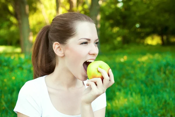 Крупный план портрет девушки кусает яблоко на открытом воздухе — стоковое фото