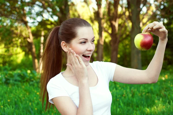 Девушка держит яблоко и выглядит удивленной, на открытом воздухе — стоковое фото