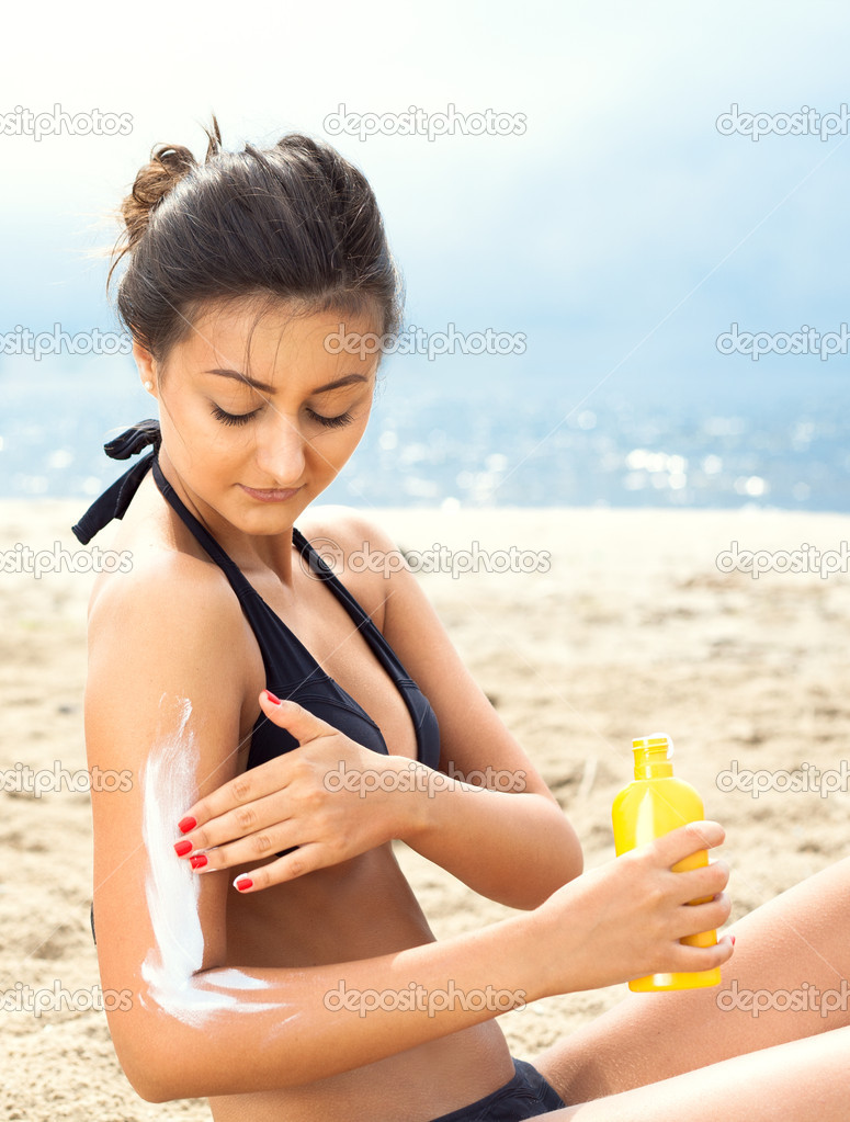 Young happy smiling beautiful tanned woman applying sun protecti