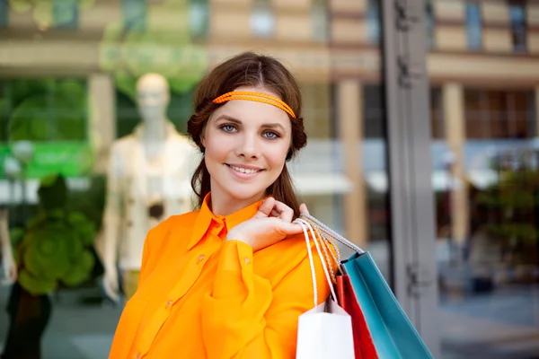 Portrait of a young woman holding shopping bags standing by a fa — Stock Photo, Image