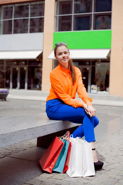 Счастливая женщина после шопинга сидела на скамейке на улице с — стоковое фото