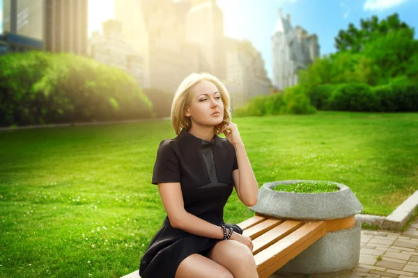 Atraktivní blondýnka mladá žena sedící na lavičce v parku nea — Stock fotografie