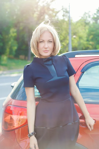 Ελκυστική ξανθιά νεαρή γυναίκα που στέκεται δίπλα της κόκκινο αυτοκίνητο και l — Φωτογραφία Αρχείου