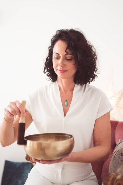 Beautiful female therapist in white uniform holding singing bowl.  Sound healing therapy concept. 