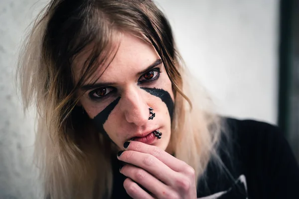 Head shot of an attractive emo punk young man looking with anger directly in camera. Close up of a pierced and face painted, long hair guy in his late 20s.