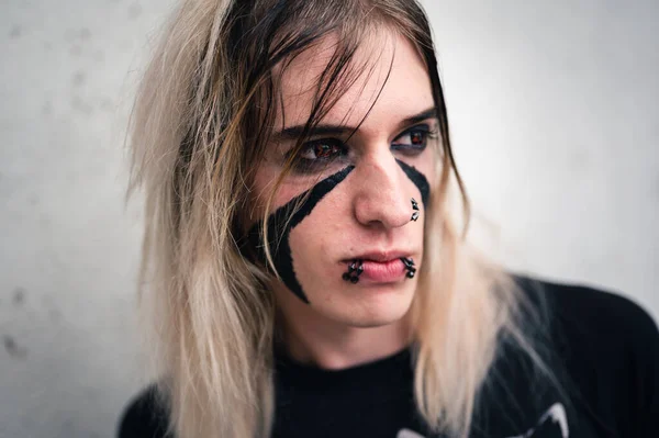 Head shot of an attractive emo punk young man with serious expression, looking away. Close up  of a pierced and face painted, long hair guy in his late 20s, isolated on white background.