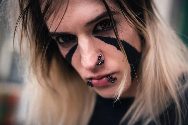 Head shot of an attractive emo punk young man looking with anger directly in camera. Close up of a pierced and face painted, long hair guy in his late 20s.