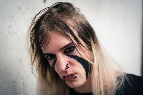 Head shot of an attractive emo punk young man looking with anger directly in camera. Close up  of a pierced and face painted long hair guy in his late 20s.
