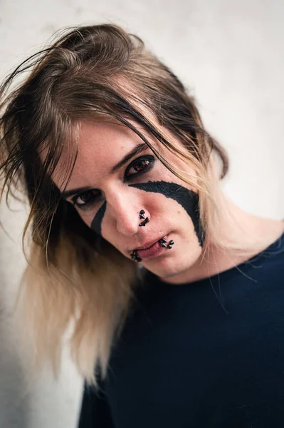 Tight headshot of an attractive emo punk young man with long hair looking directly in camera. Close up of a pierced and face painted guy in  his late 20s posing in a seductive way.