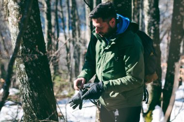 Çekici beyaz sakallı adam ormanda yürüyüş macerasında eldiven takmış. Genç yürüyüşçü kışın sonlarına doğru dağ ormanlarından geçiyor.. 