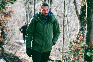 Ormanda yürüyüş yapan çekici beyaz bir erkek. Genç yürüyüşçünün portresi dizlerinden yukarı doğru dağ ormanlarında kışın sonlarına doğru yokuş yukarı yürüyor.. 