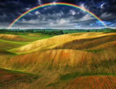 Rainbow and dramatic gray sky with clouds landscape. picturesque hilly field