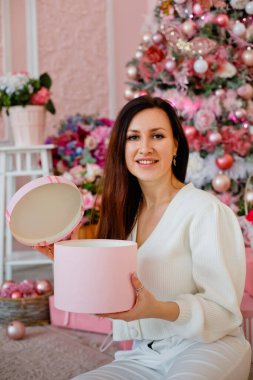 Noel ağacının yanında hediye kutusuyla gülümseyen genç bir kadın. Kız elinde bir hediye tutuyor..