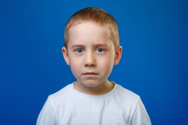 Mavi arka planda beyaz tişörtlü üzgün bir çocuk. Metin için yer