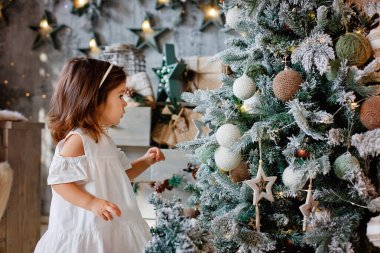 Çekici küçük bir kız evinde balonlarla bir Noel ağacını süslüyor..