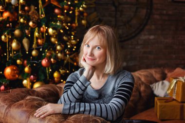 Güzel bir genç kadın bir Noel ağacı ve bir saatin arka planında oturuyor. Fotoğrafçılığın seçici odak noktası